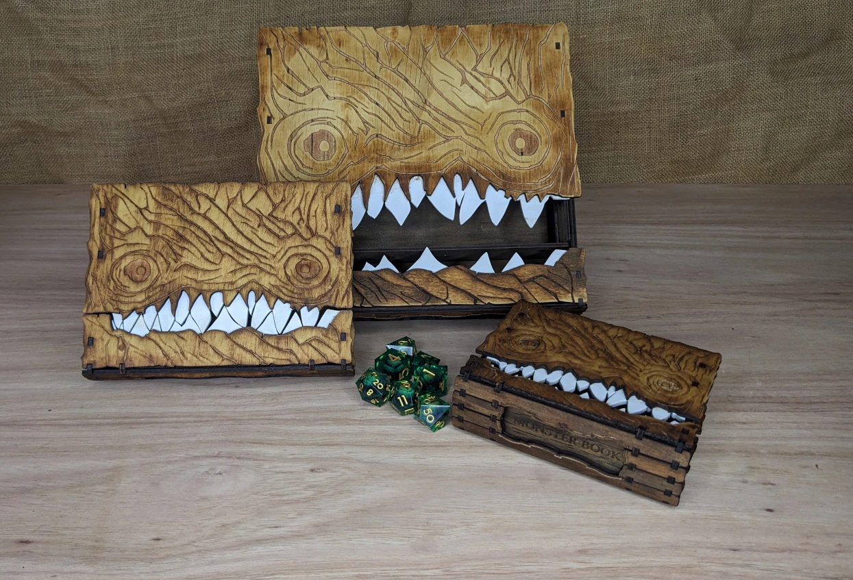 Collection of handcrafted wooden monster book boxes in small, medium and large sizes, displayed with tabletop gaming dice.