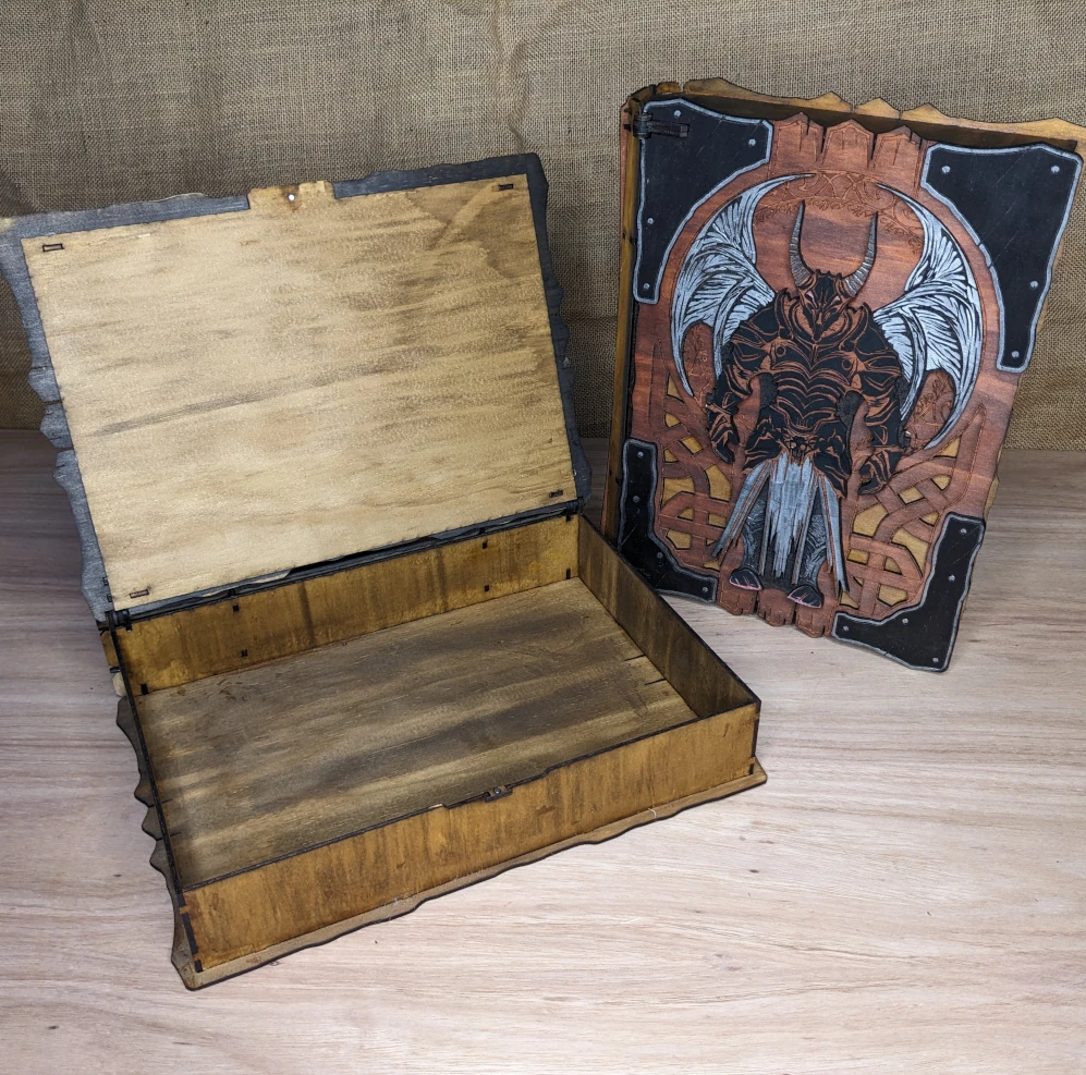 Open engraved wooden book box showing fabric-lined interior, handmade fantasy storage box for dice or keepsakes